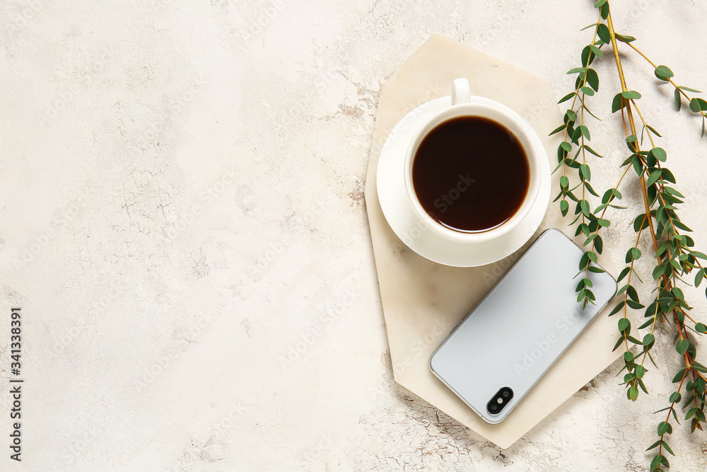 Cup of coffee, mobile phone and green branches on light background