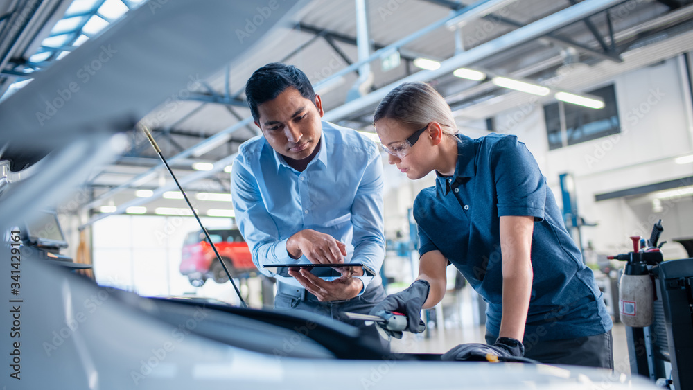 Instructor with a Tablet Computer is Giving a Task for a Future Mechanic. Female Student Inspects th