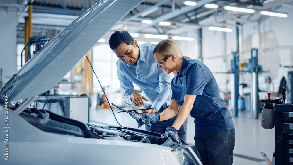 Instructor with a Tablet Computer is Giving a Task for a Future Mechanic. Female Student Inspects th