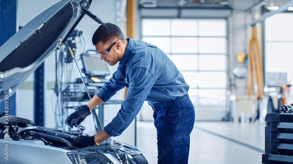 Professional Mechanic is Working on a Car in a Car Service. Repairman in Safety Glasses is Working o