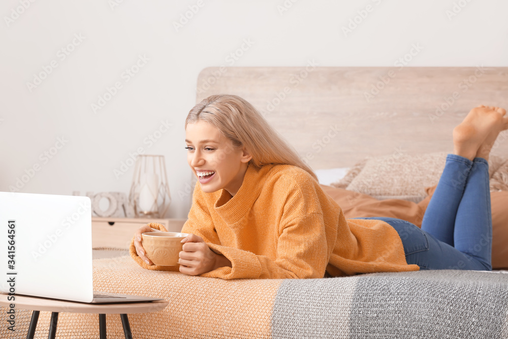 Beautiful young woman with laptop drinking tea at home