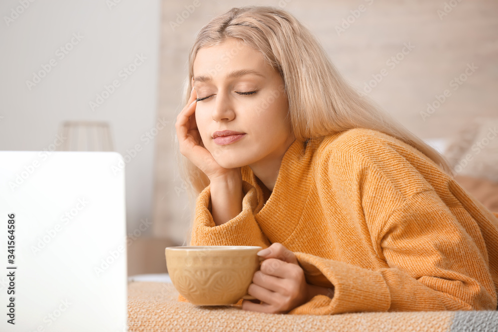 Beautiful young woman with laptop drinking tea at home