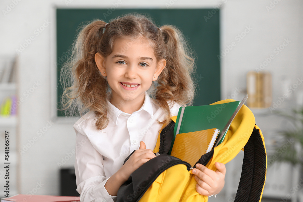 Cute little schoolgirl with backpack in classroom