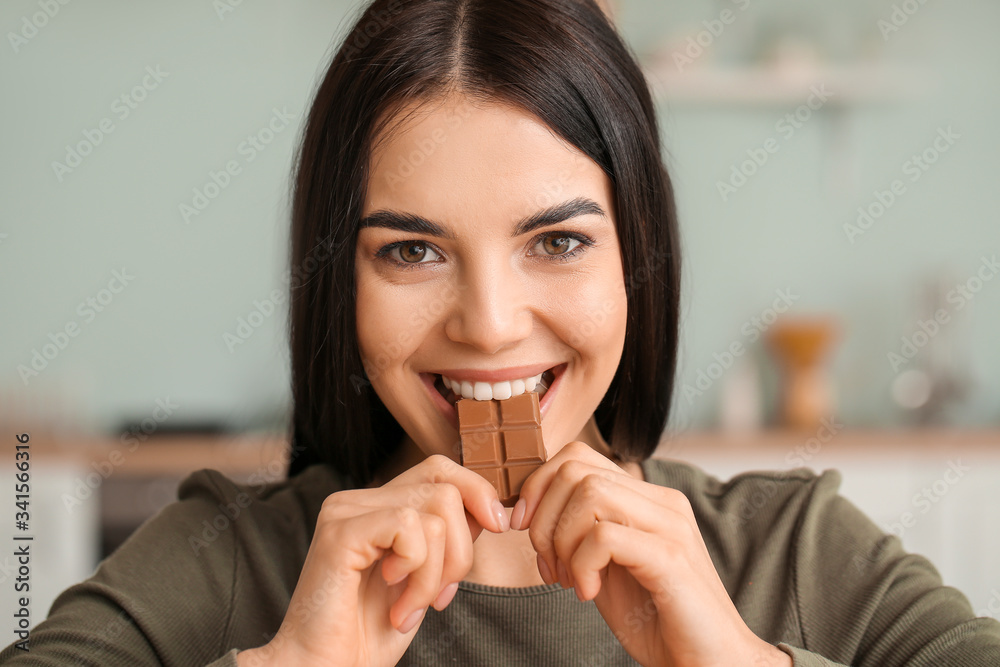 Beautiful young woman eating chocolate in kitchen