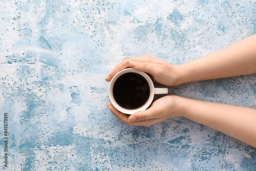 Female hands with cup of hot coffee on color background, top view