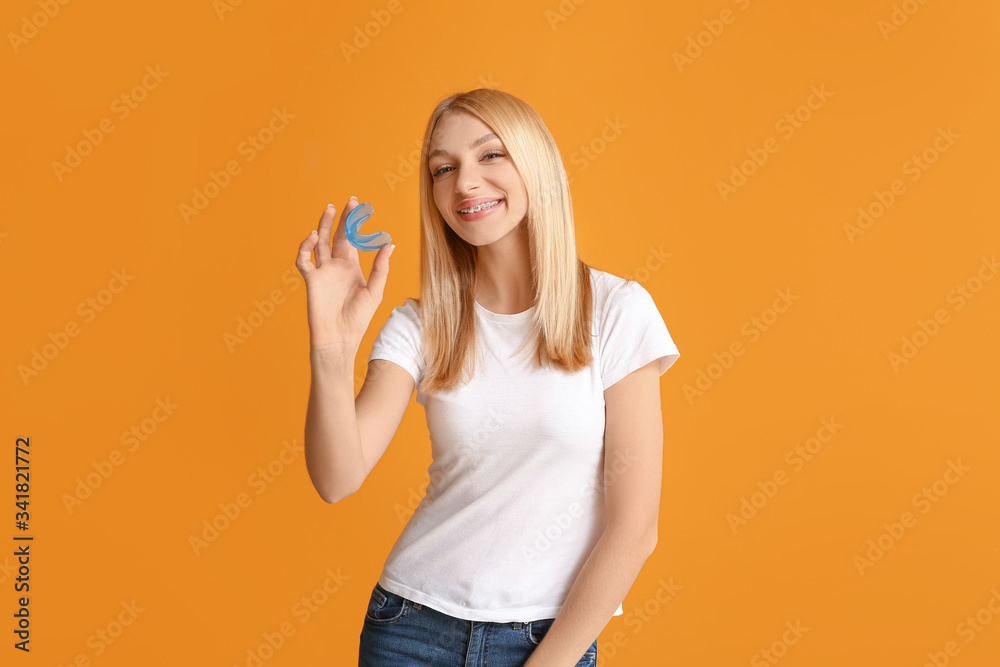 Young woman with dental braces and mouth protector on color background