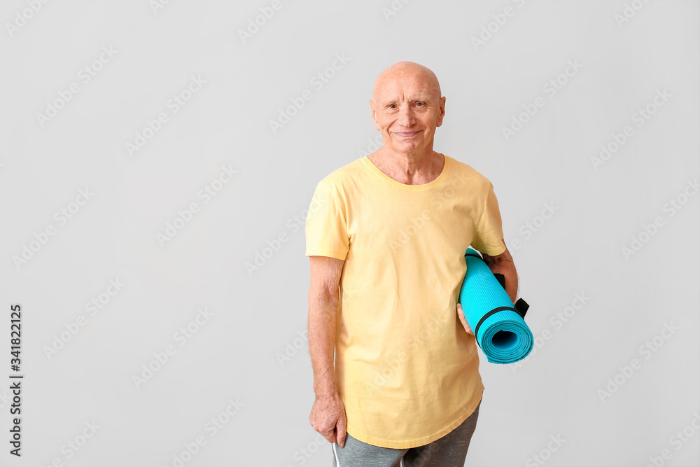 Sporty elderly man with yoga mat on light background