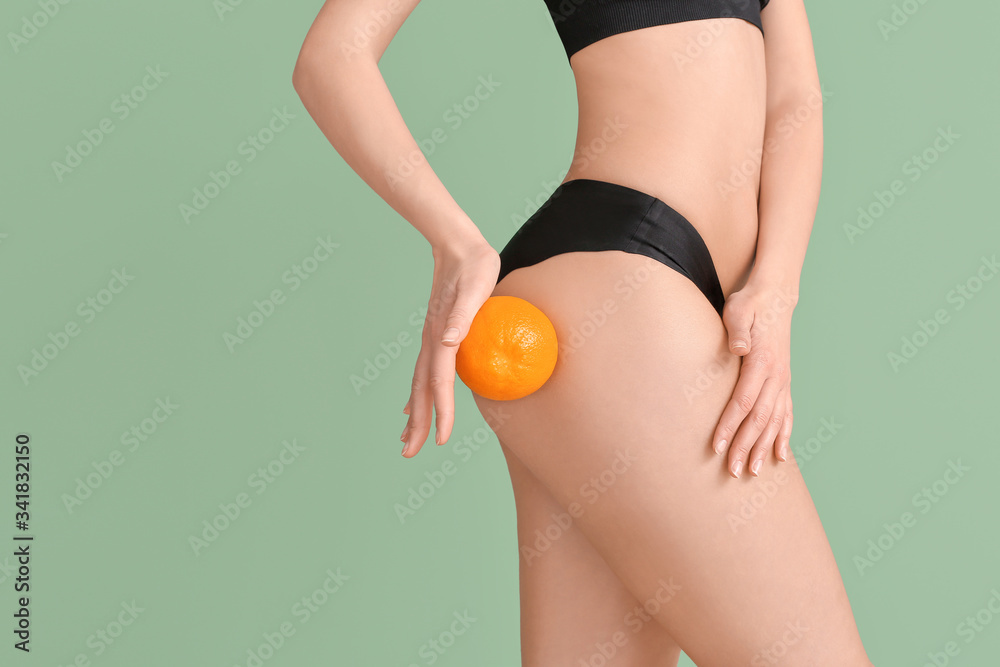 Young woman with orange fruit on color background. Concept of cellulite