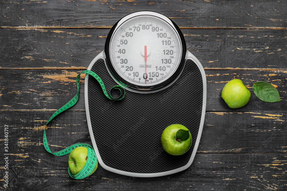 Weight scales with measuring tape and apples on wooden background. Slimming concept