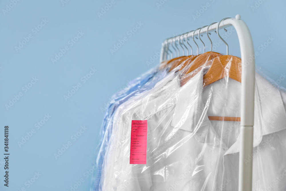 Rack with clothes after dry-cleaning on color background