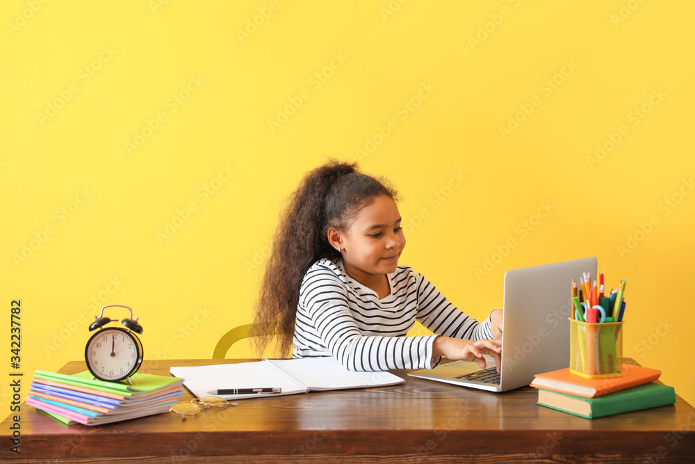 Little African-American girl doing homework against color background