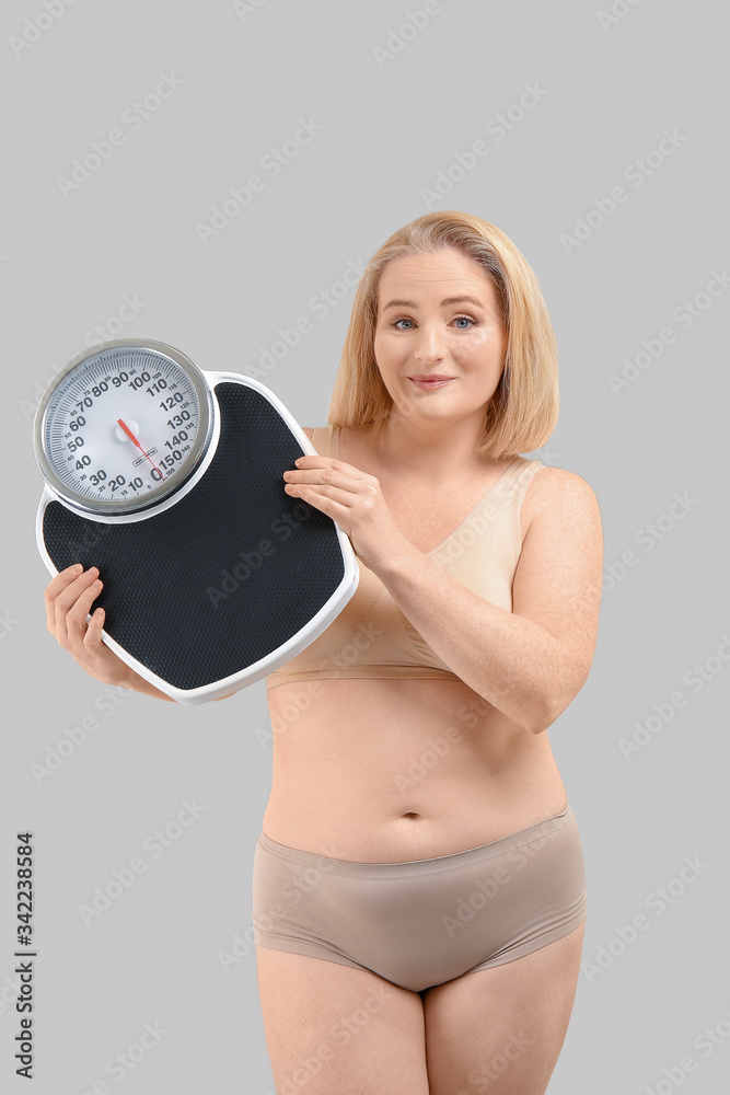 Overweight woman with scales on grey background. Weight loss concept