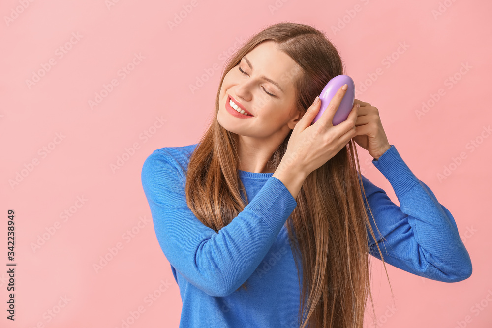 Beautiful young woman brushing hair on color background