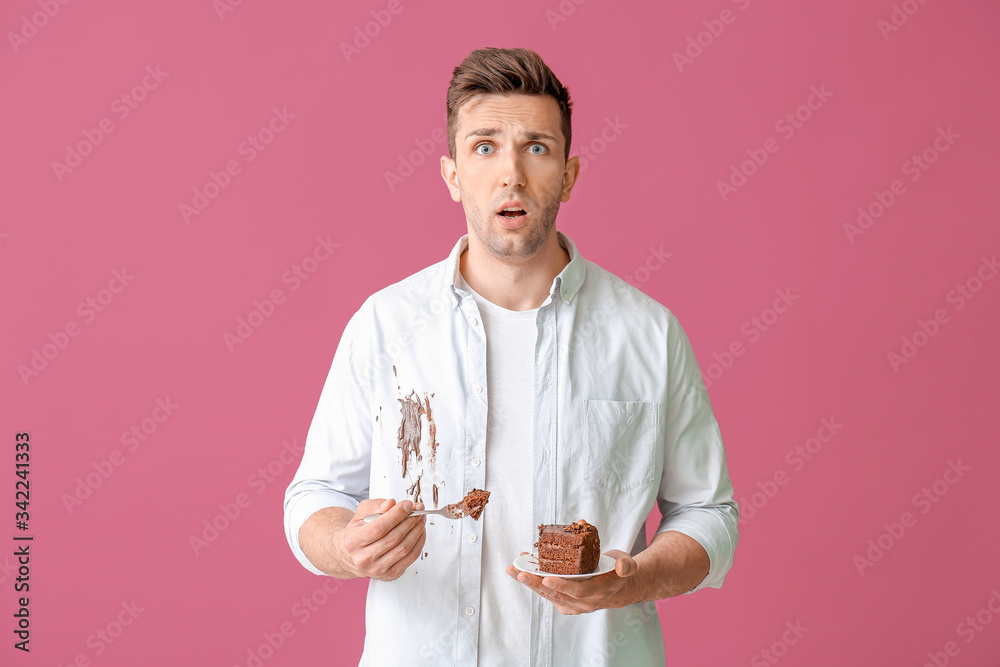 Troubled man in dirty clothes eating chocolate cake on color background