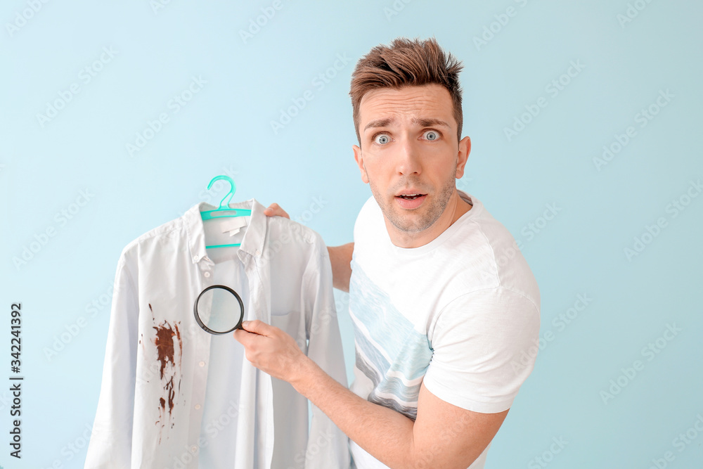 Troubled man with dirty clothes and magnifying glass on color background