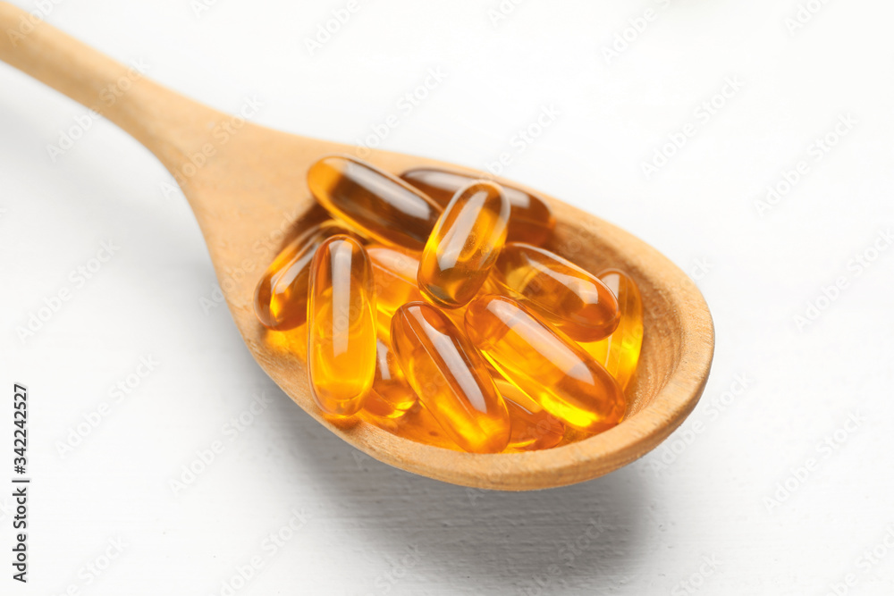 Spoon with fish oil capsules on white wooden background