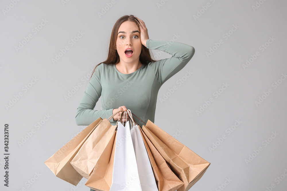 Surprised young woman with shopping bags on grey background