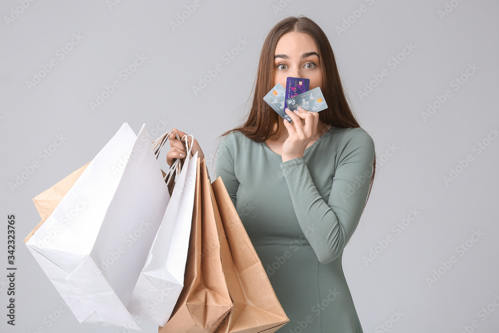 Young woman with shopping bags and credit cards on grey background