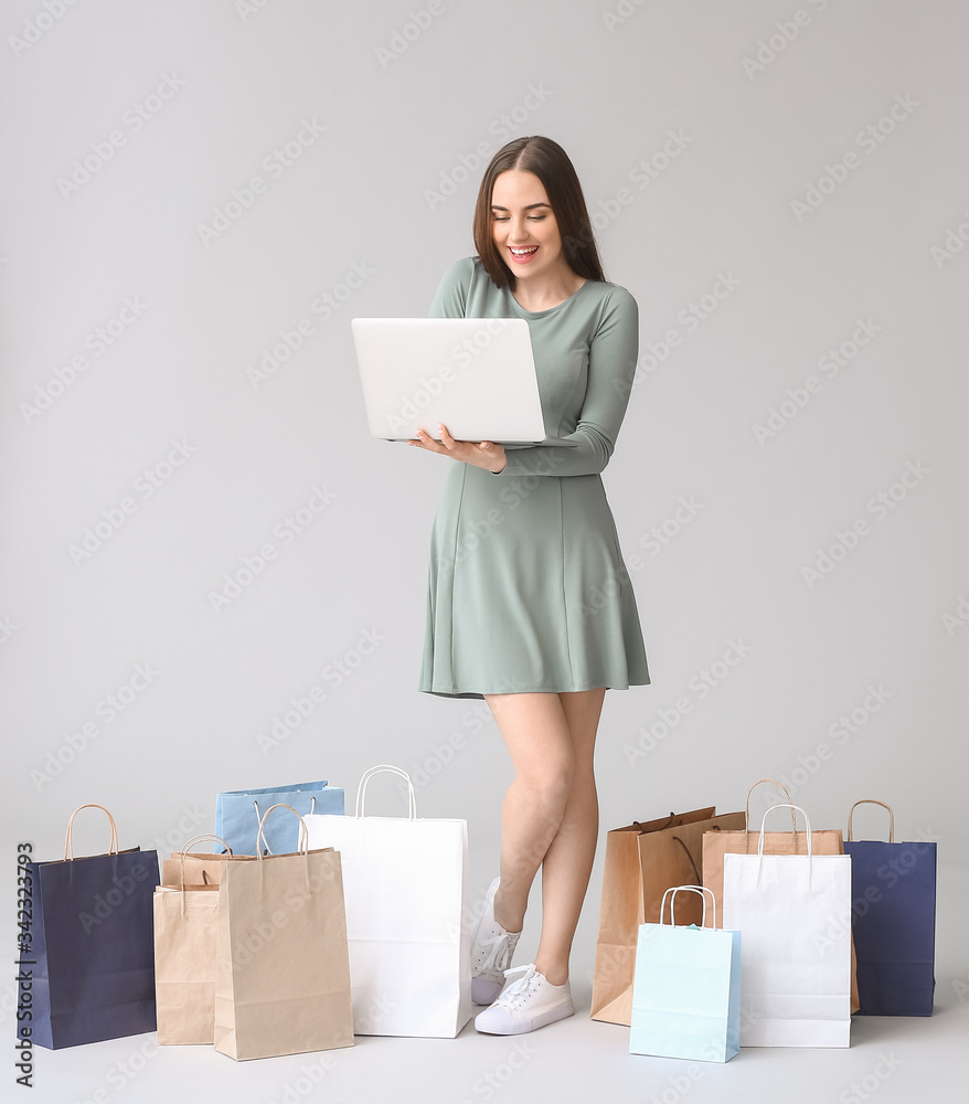 Young woman with laptop and shopping bags on grey background