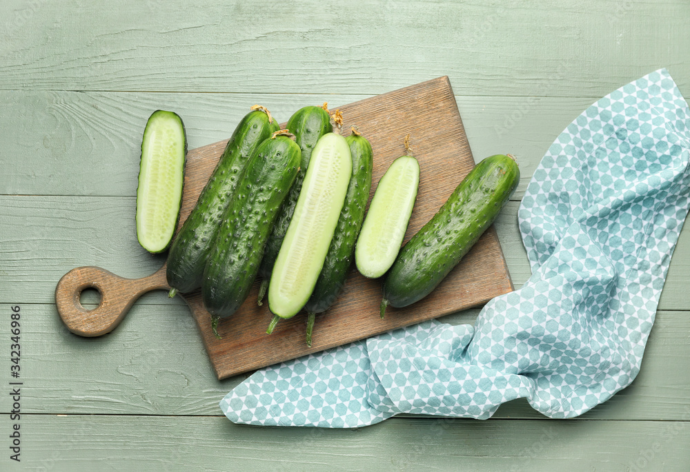 Board with green cucumbers on wooden background