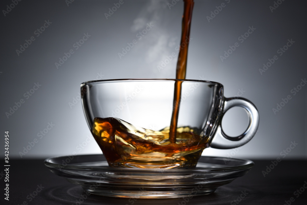 Pouring coffee with smoke on a transparent cup on black background