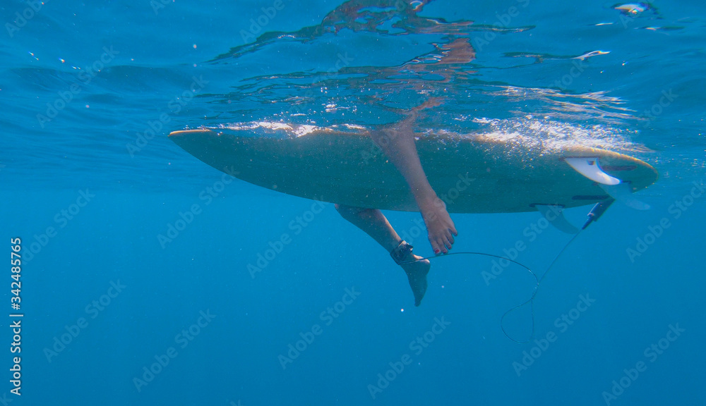 UNDERWATER: Surfer girl sits and rests on surfboard on while on a surfing trip.