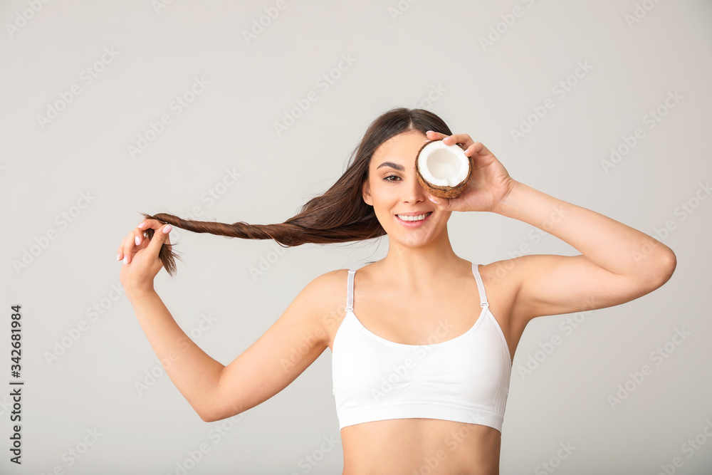 Beautiful young woman with long hair and coconut on grey background