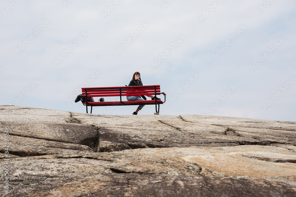 A huge stone, on which among the trees stands a lonely bench, a bench against the blue sky