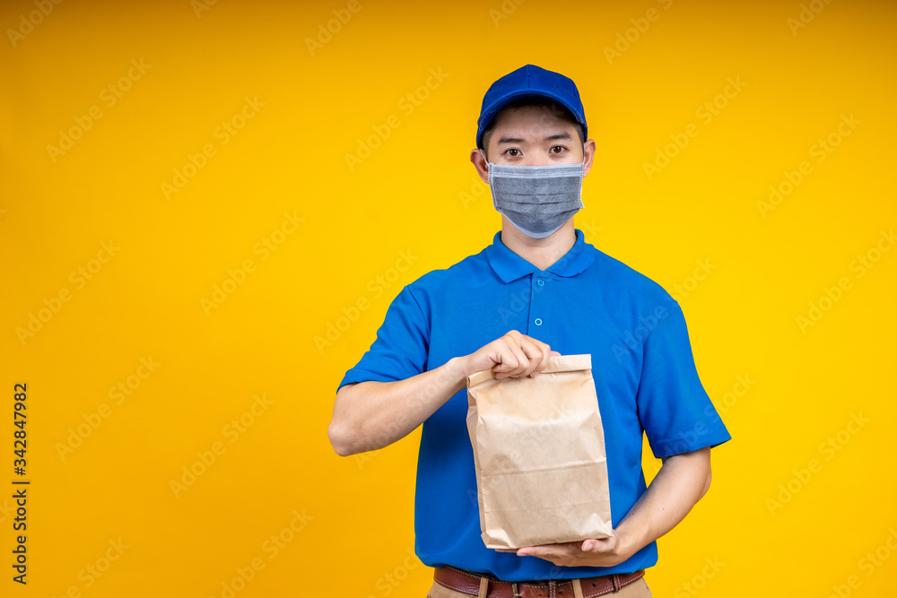 Young Asian delivery man holding food or pizza box and showing application on mobile over yellow iso