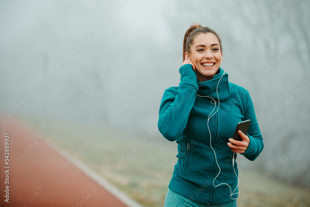 Young fit girl in sportswear is listening to the music while doing her cardio outside.