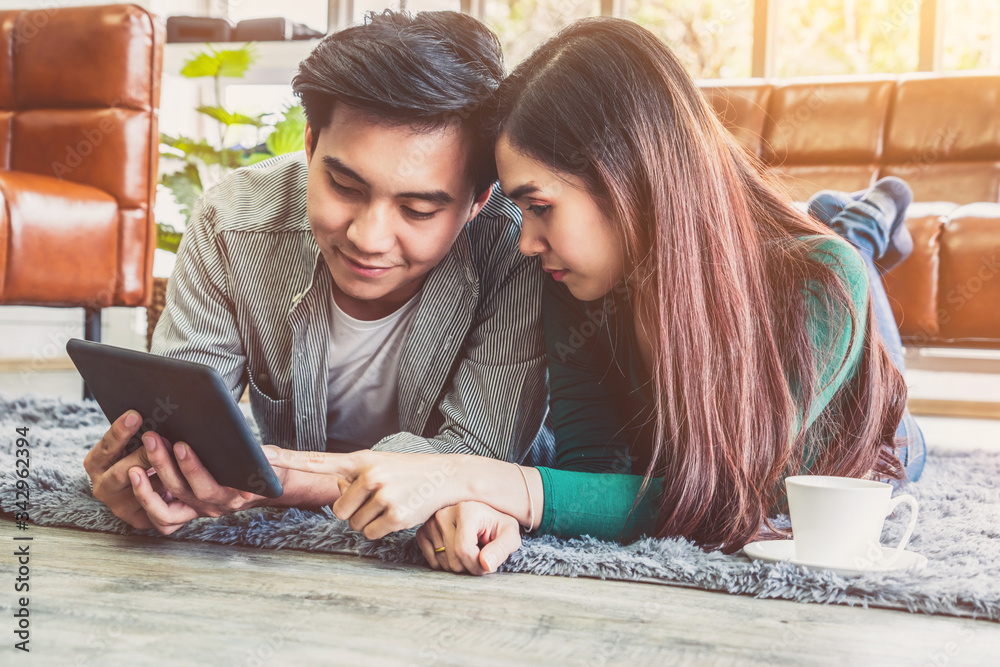 Happy Asian couple use tablet while lying down on carpet at living room floor. Love and relationship