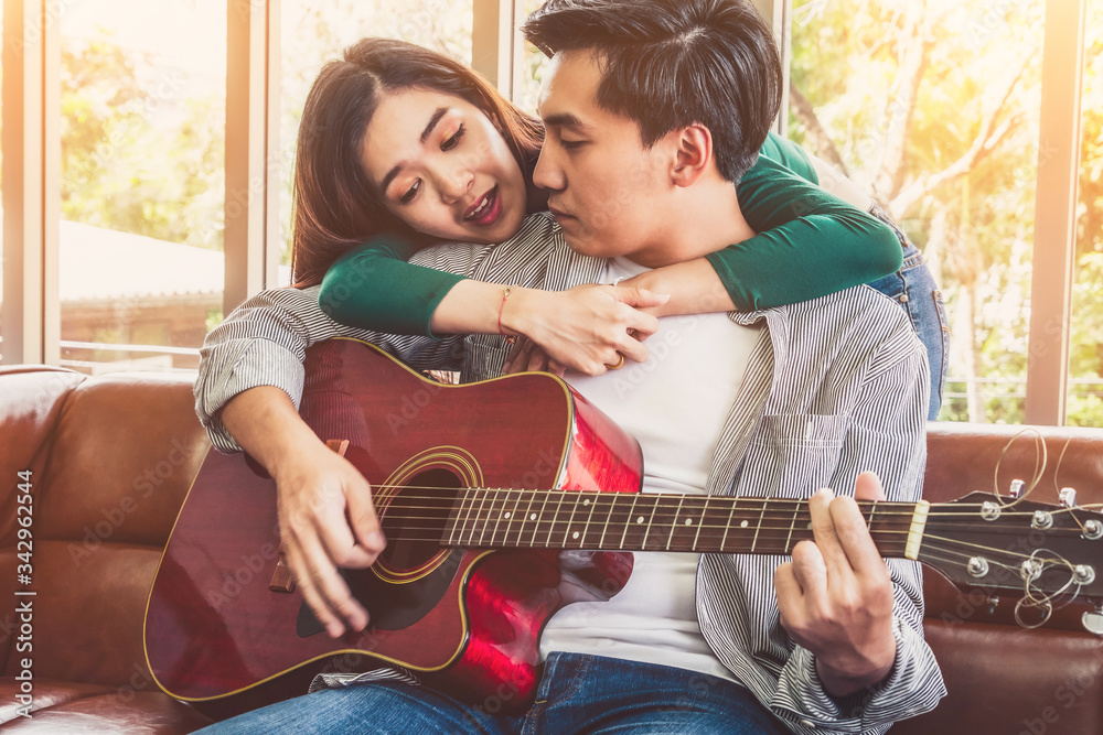 Young Asian Couple Plays Guitar and Sing Song in Living Room at Home Together. Music and Lifestyle c