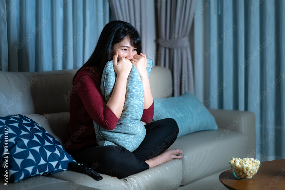 Young asian woman watching television suspense movie or news looking shocked and excited eating popc