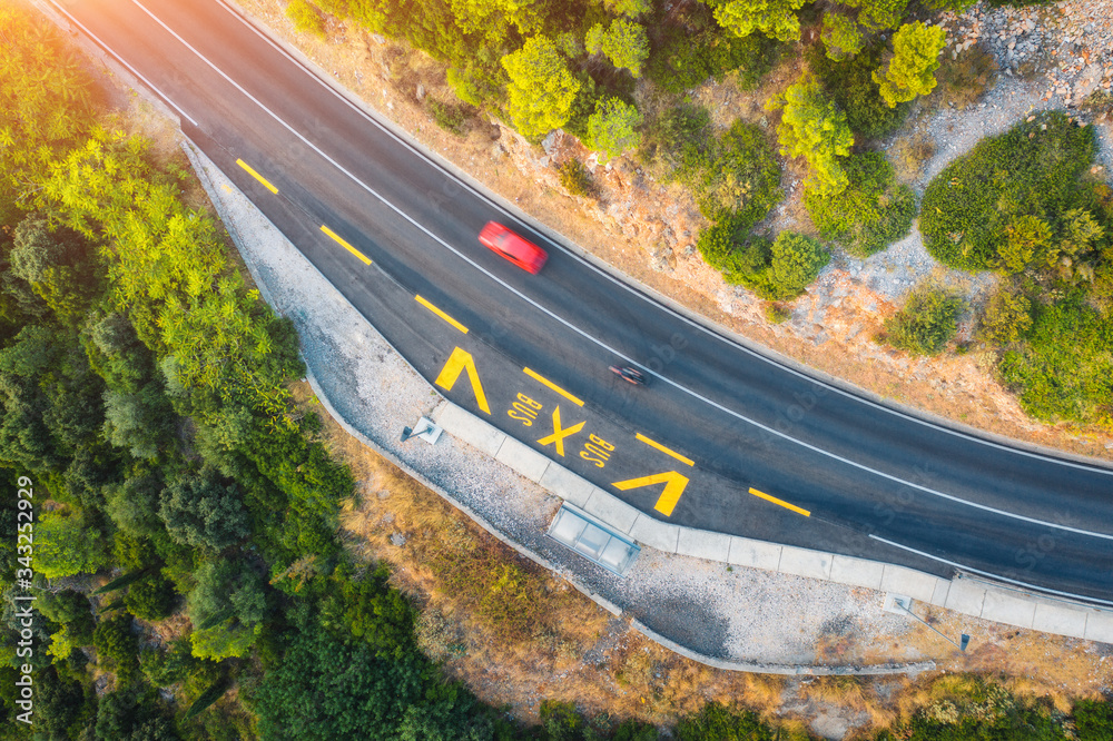 夏日日落时，美丽的绿色森林中的道路鸟瞰图。红色汽车o的彩色景观