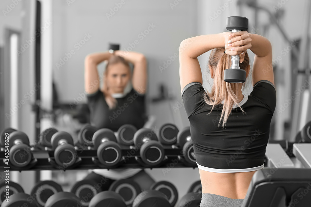 Sporty young woman training with dumbbells in gym