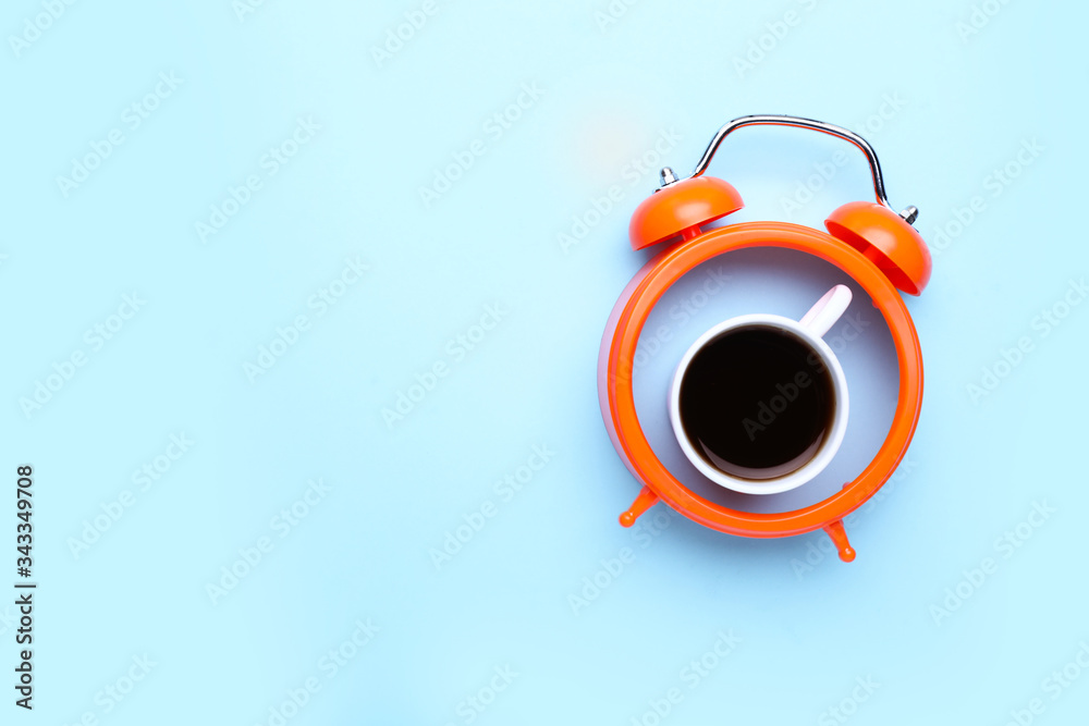 Cup of coffee with alarm clock on color background