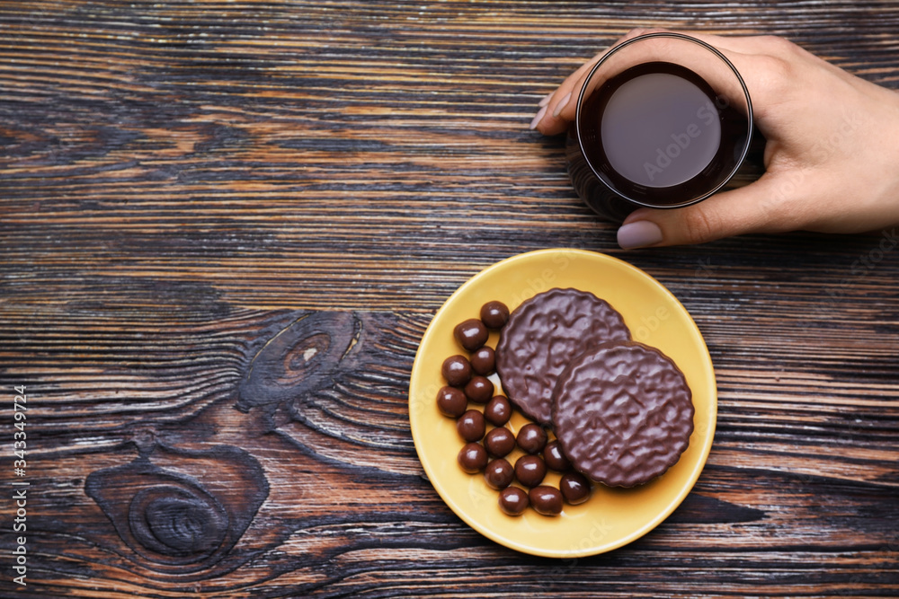 Female hand with glass of coffee and sweets on wooden background