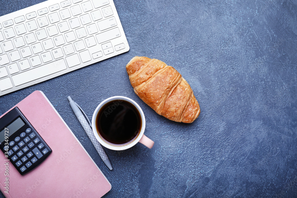 Cup of coffee with croissant, computer keyboard, calculator and notebook on dark background