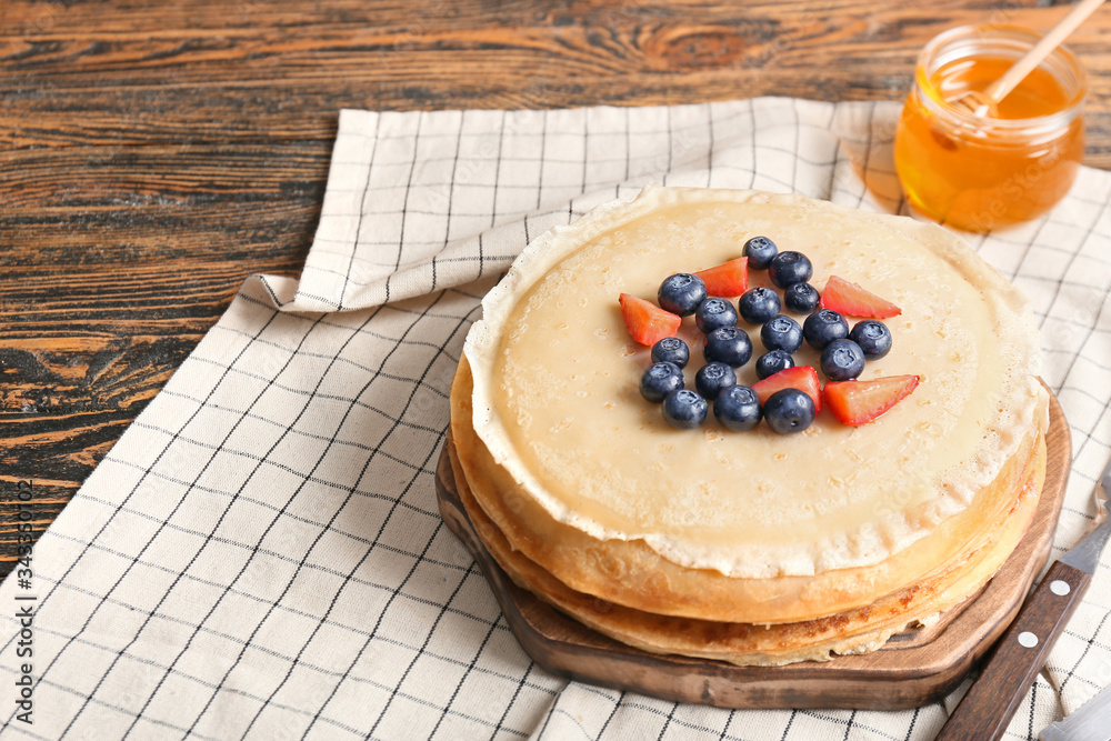 Board with tasty blini and berries on table