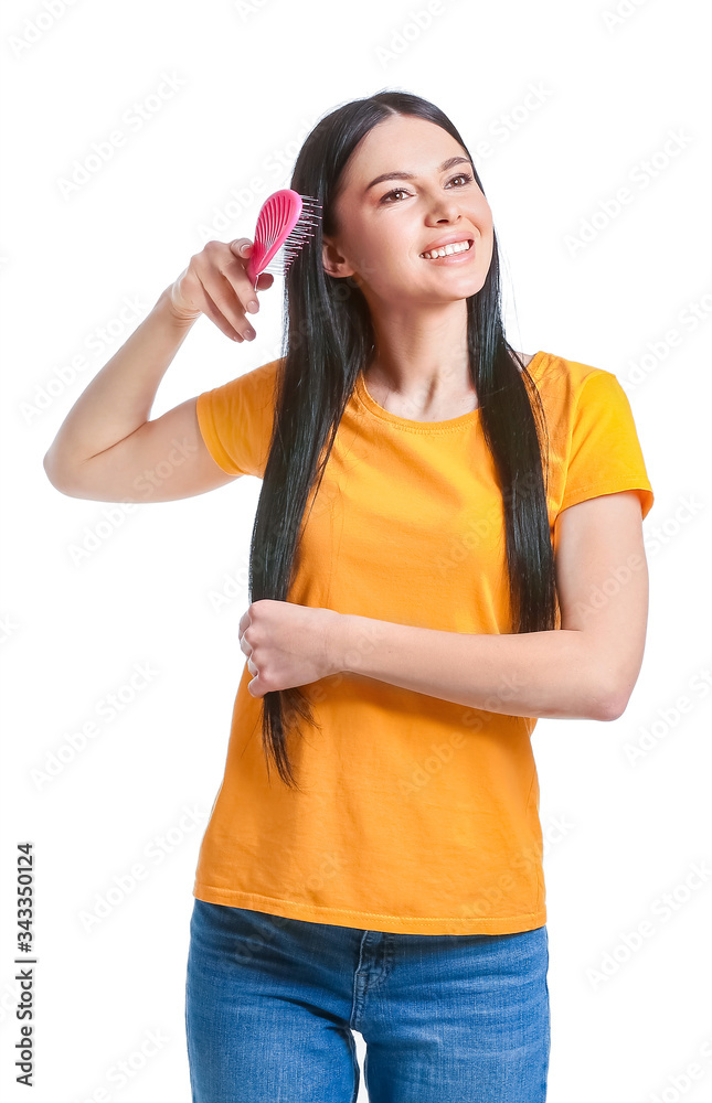 Beautiful young woman brushing hair against white background