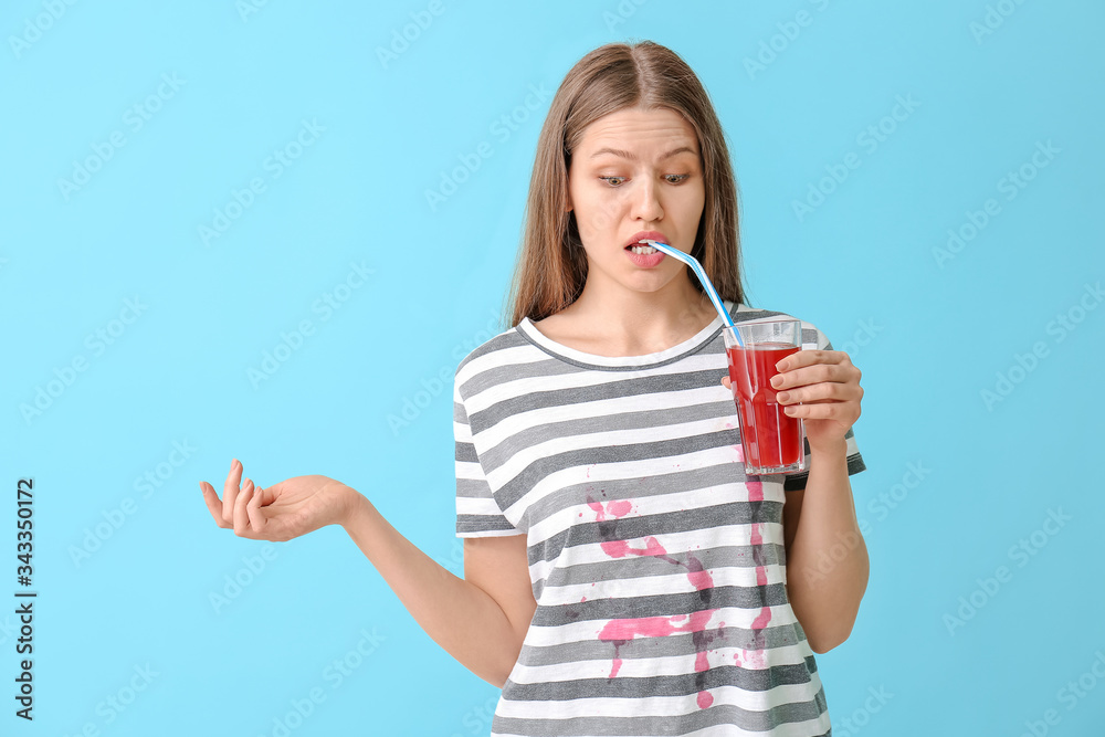 Woman in dirty clothes drinking juice on color background