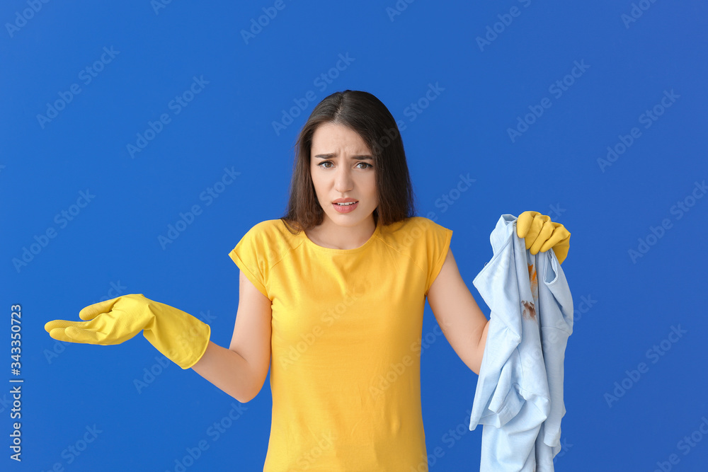 Displeased young woman with dirty clothes on color background