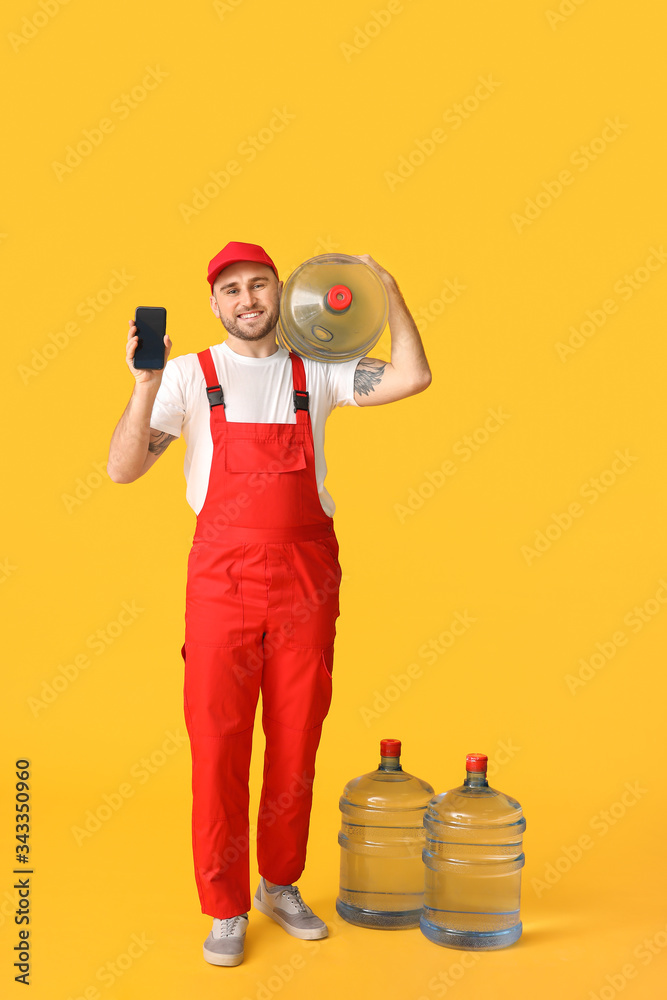 Delivery man with bottles of water and mobile phone on color background