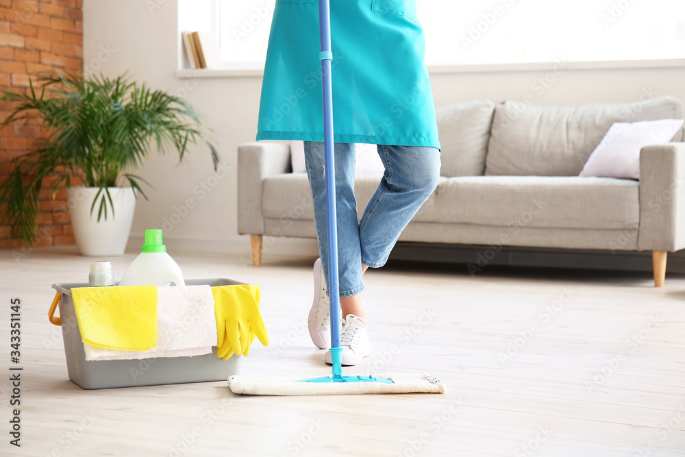 Young woman mopping floor in room