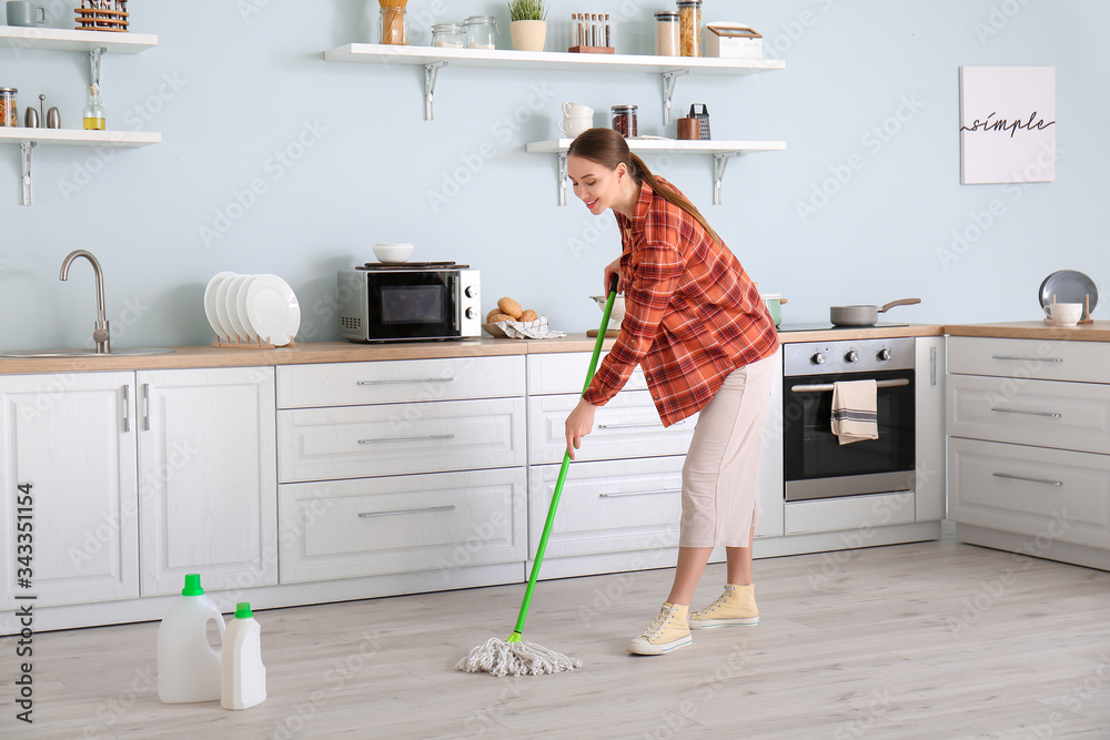 Young woman mopping floor in kitchen