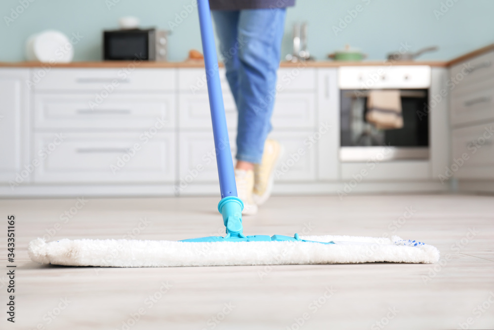 Young woman mopping floor in kitchen