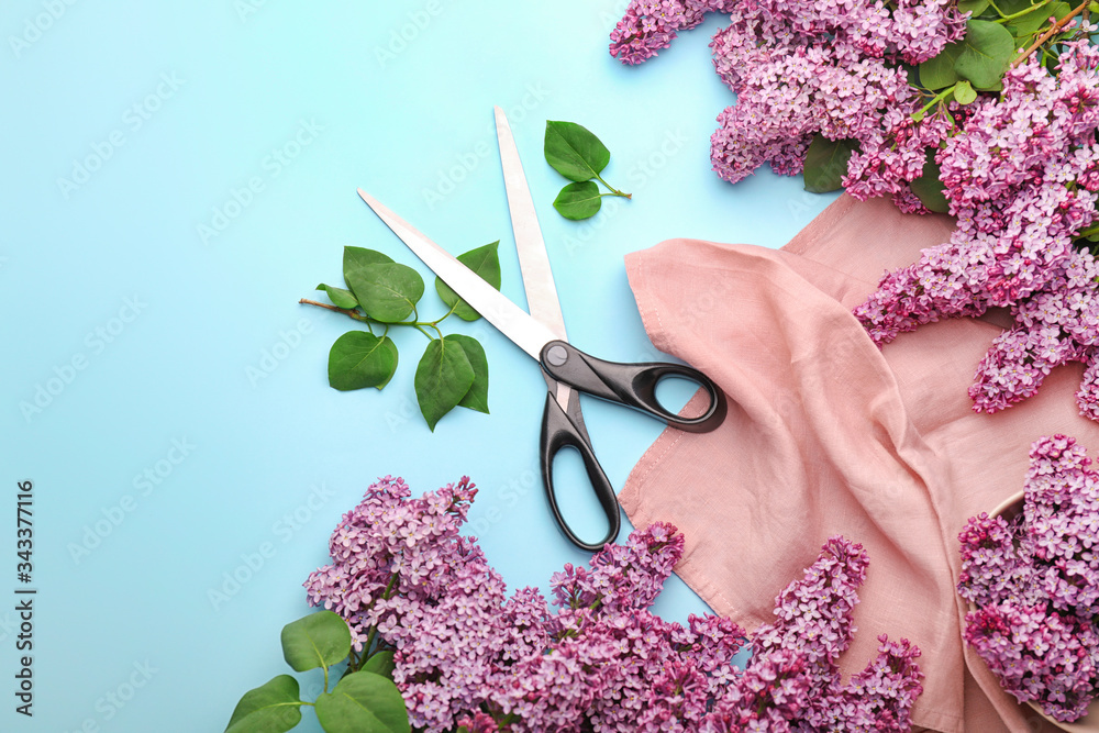 Beautiful lilac flowers, cloth and scissors on color background