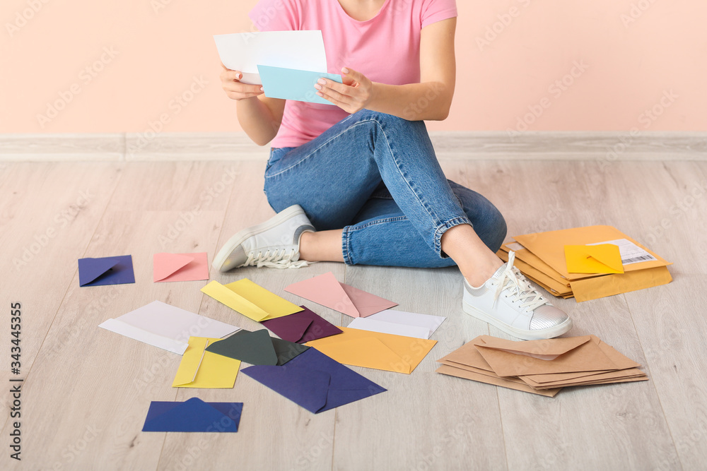 Young woman with many letters sitting near color wall