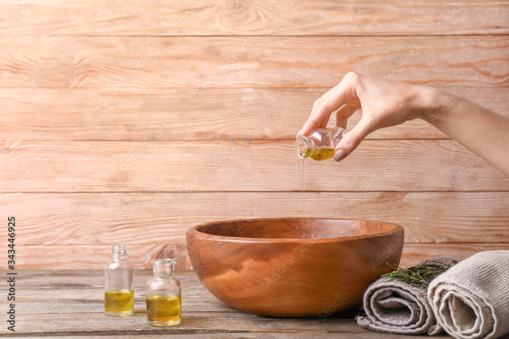 Woman pouring essential oil from bottle into bowl on wooden background