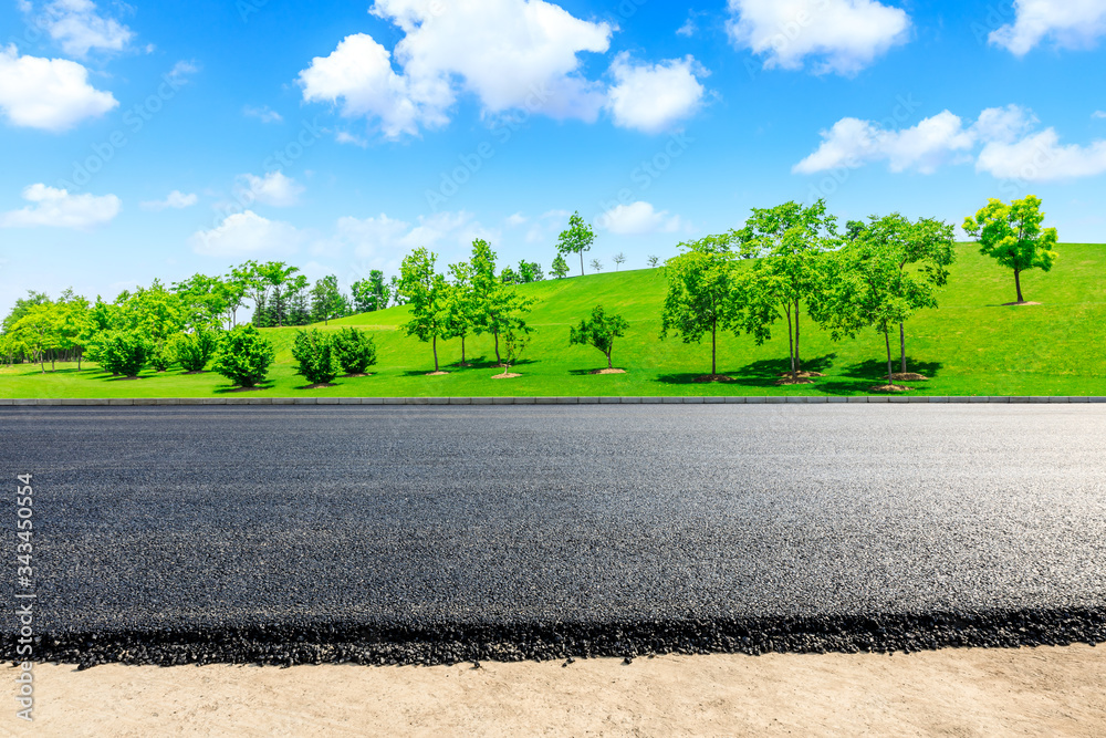 Empty asphalt road and green grass with tree under the blue sky.